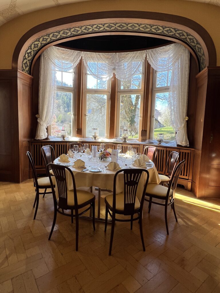 Villa Commerell – stilvoll feiern im kleinen Kreis Die Villa Commerell ist ein kleiner, eleganter Raum für besondere Anlässe. Er hat große Fenster mit viel Licht, eine schöne alte Decke und dunkles Holz an den Wänden. Die runden Tische sind fein gedeckt – mit Gläsern, Stoffservietten und frischen Blumen. Gut geeignet für: kleine Feiern oder Empfänge ruhige Essen im Familienkreis besondere Gäste und Geschäftstreffen
