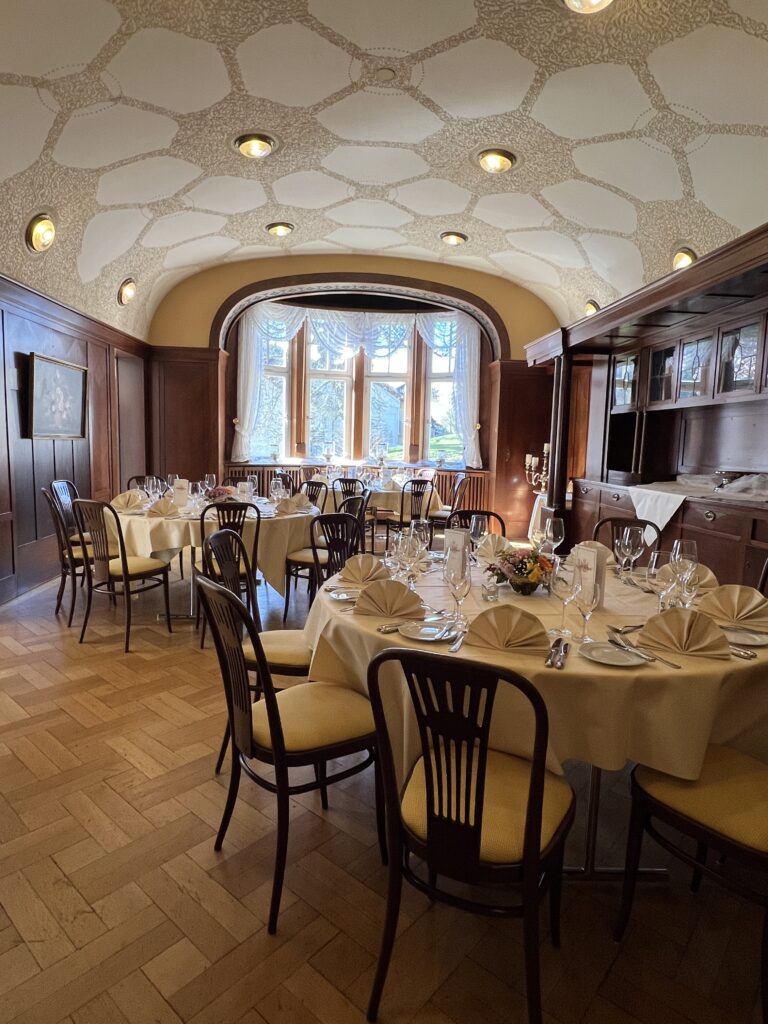 Villa Commerell – stilvoll feiern im kleinen Kreis Die Villa Commerell ist ein kleiner, eleganter Raum für besondere Anlässe. Er hat große Fenster mit viel Licht, eine schöne alte Decke und dunkles Holz an den Wänden. Die runden Tische sind fein gedeckt – mit Gläsern, Stoffservietten und frischen Blumen. Gut geeignet für: kleine Feiern oder Empfänge ruhige Essen im Familienkreis besondere Gäste und Geschäftstreffen